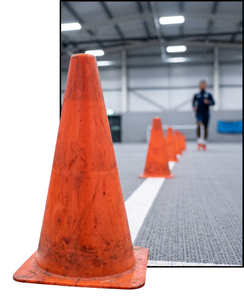 An ordinary training cone standing on a line as a runner passes behind it